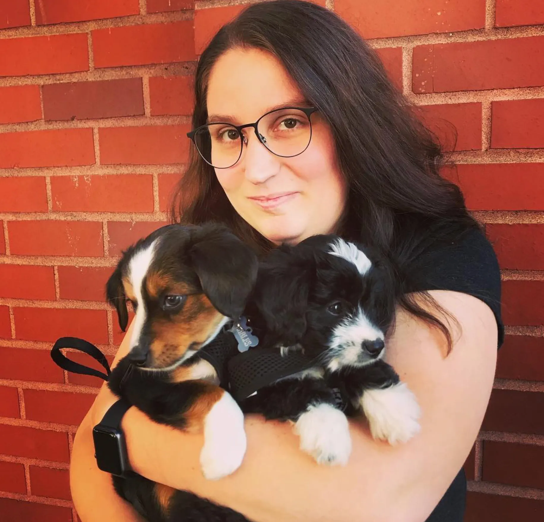 Jordan standing in front of a brick wall with two puppies in her arms.